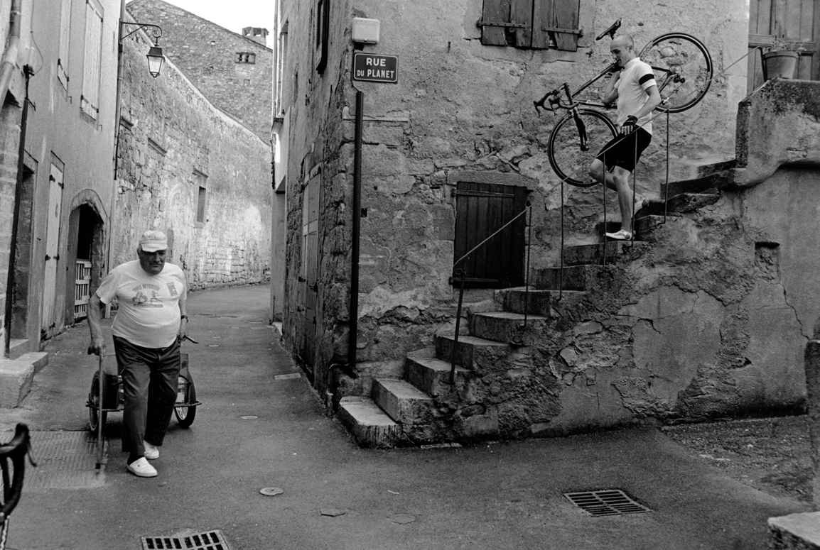 Cyclist carrying bike through French village